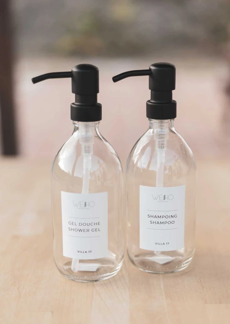 Deux flacons en verre transparent à pompes noires, étiquettes au logo Weho, Gel douche shower gel et Shampoing shampoo, mention Villa 17