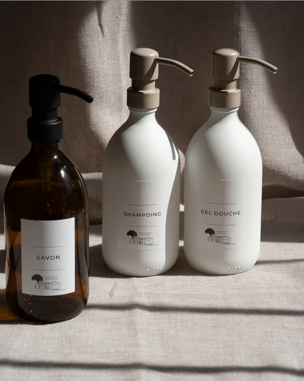 Distributeurs de savon en verre ambré et blanc, étiquetés savon, shampoing et gel douche