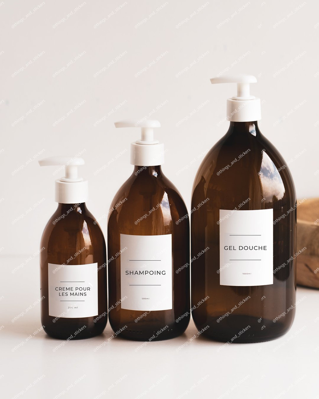 Trois distributeurs en verre ambré : crème pour les mains, shampoing, gel douche