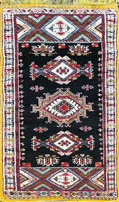 Vertical, top facing image of vintage Moroccan rug, showing the geometric pattern with many medallions in various colors of red, blue and gold.