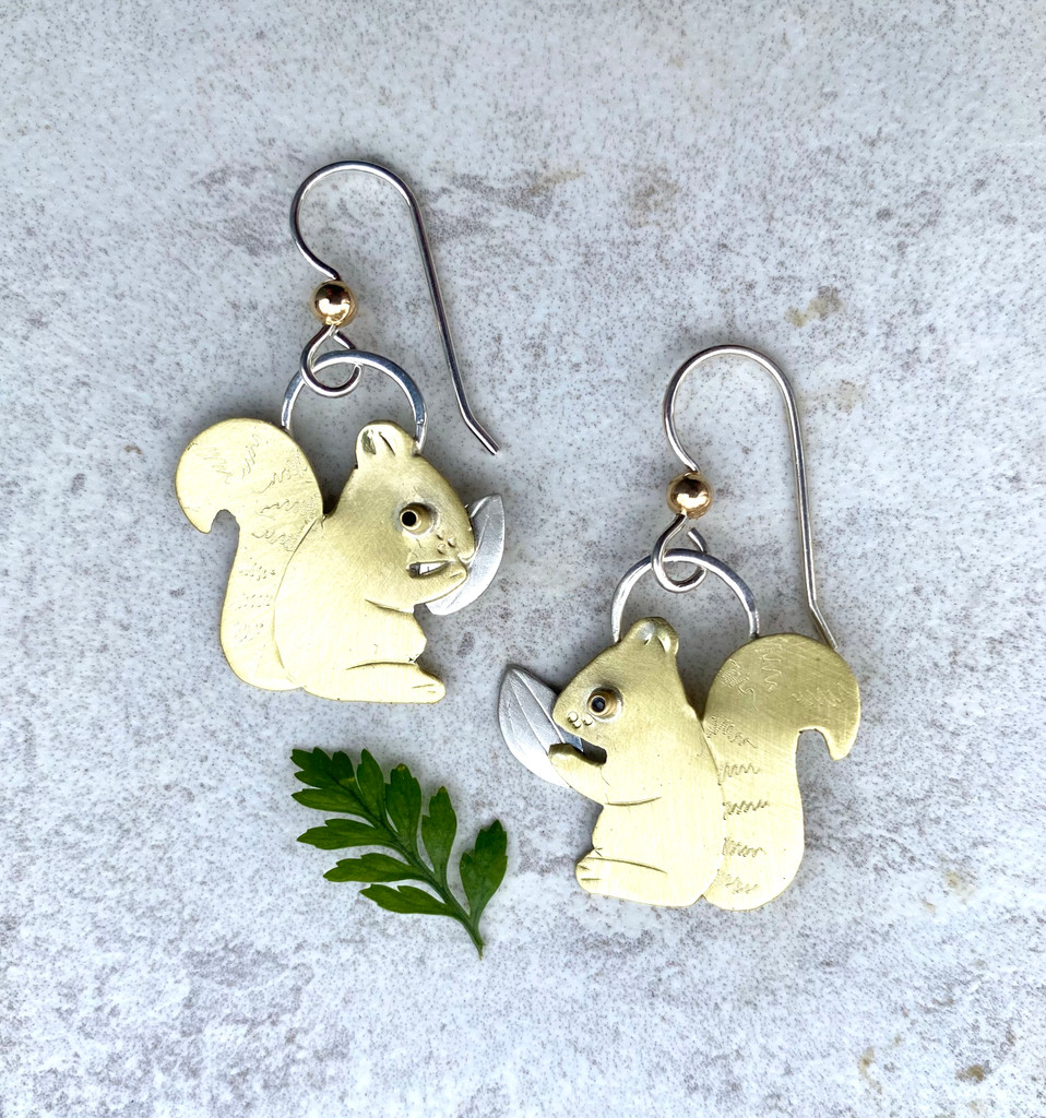 Squirrels are the monkeys of North America. They jump from tree to tree, and both play and squabble. Although something of an albatross when it comes to birds and feeders, they are ultimately compelling little critters. These Squirrel Friend Earrings celebrate them. They are handcrafted out of jeweler's brass and Sterling. They measure 1" by 1", not including the Sterling earring wires. They are lightweight and fun to give and to wear. 