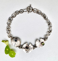 Anyone who has spent any time in a pond with lily pads (yup, I'm in that club) knows that frogs do, indeed, like to sit on them. This chain bracelet celebrates that fact. It features 3 lily pads . One is set with a lovely green peridot, one with a blue topaz, and the middle one has a silver carved (not cast!) frog basking in the sun. The links that create the chain are swirls of silver that echo the movement of water. Each link is attached by 2 jump rings, which give it stability. It has a me-made toggle clasp which makes it really easy to put on and take off by oneself. It measures 7 1/2" long which should fit most wrists. 