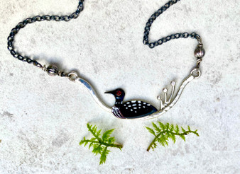 The sign and sound of a loon is always special and this necklace is a reminder of that. It features a swimming loon and is a tribute to a majestic bird that has made a remarkable comeback. It is is handcrafted out of Sterling silver and jeweler's brass, and is suspended from an oxidized Sterling chain. It measures 18" which includes the 2" focal piece. 