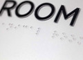 ADA Braille text and dots on a replacement lens for curved sign