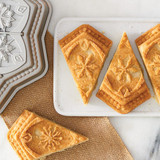 Snowflake shortbread cookies on a platter with snowflake shortbread pan in upper left hand corner.