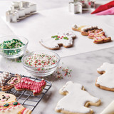 Process image of decorating cookies. Cookies on cooling racks. Upper right hand corner shows pastry bags with red and pink icing.