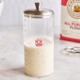 Petite Sourdough Crock with sourdough starter inside. The crock is setting on a countertop with a bag of King Arthur All-Purpose Flour.