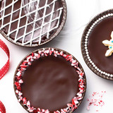 3 Chocolate Indulgence Cake mix baked in the Bakeable Paper Large Round Pans and Lids. One cake decorated with crush peppermint candy. One cake decorated with with cris-cross icing. One cake decorated with a white star in the center.
