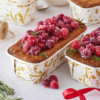 Fruitcake baked in the Gold Filigree Bakeable Paper Loaf Pans. Fruitcake has candied cranberries on top.