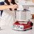 Red Ankarsrum stand mixer with person using bowl scraper to add ingredients to mixer bowl.