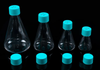 Four clear plastic Erlenmeyer flasks with teal vented screw caps and extra caps in front, on a black background.
