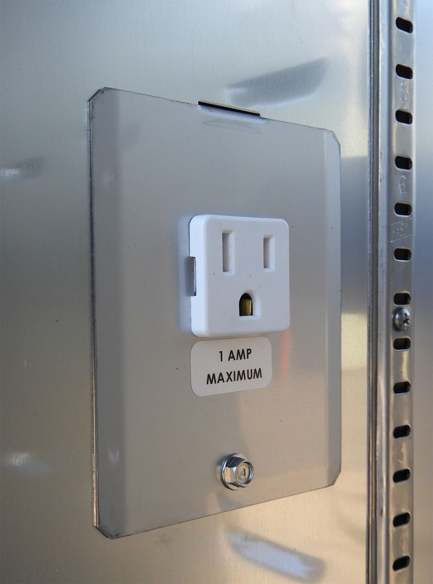 Close-up of a white electrical outlet with a "1 Amp Maximum" label on a metal panel.