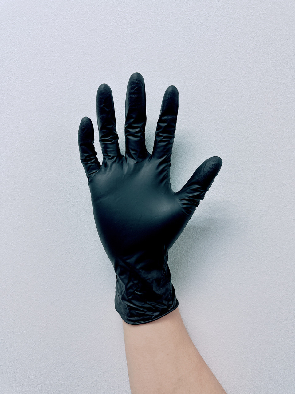 A hand wearing a black textured nitrile examination glove against a white background.