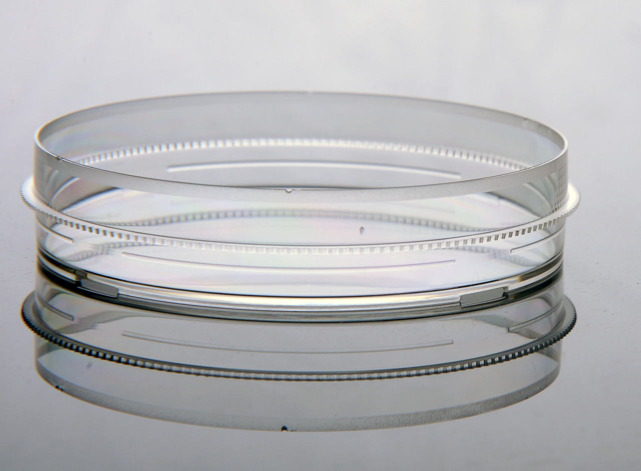 Clear polystyrene cell culture dish with a gripping ring, shown at eye level against a grey background with its reflection.