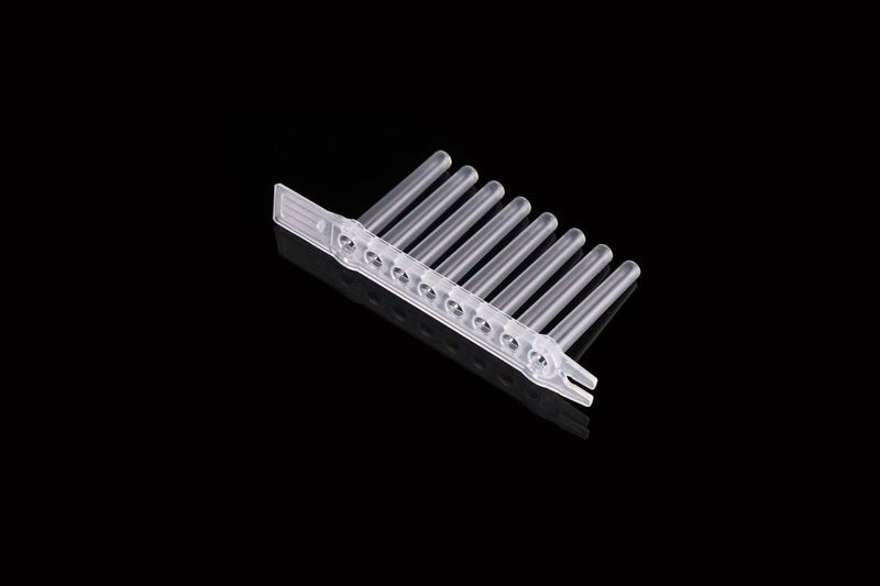 An 8-strip clear plastic comb for laboratory use, viewed at a high angle against a black background.
