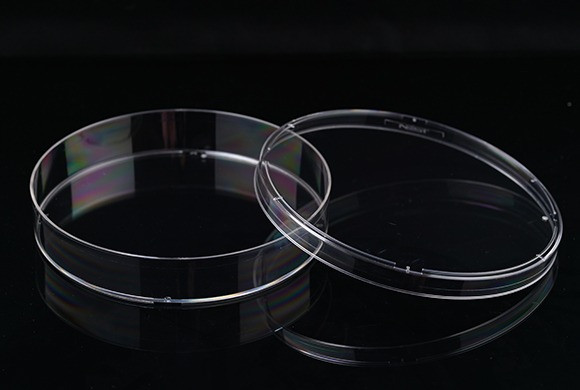 Clear plastic NEST cell culture dish and lid lying side by side on a black surface.
