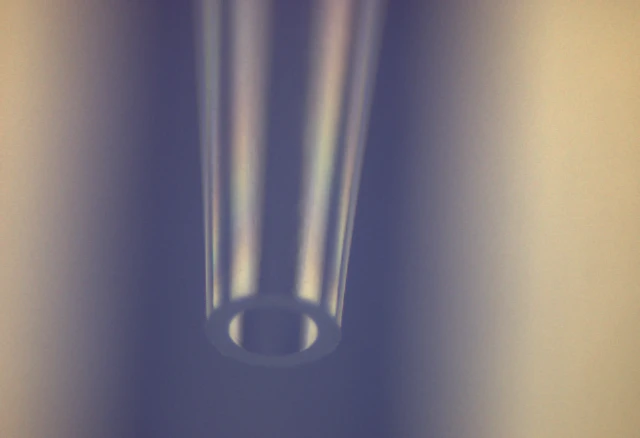 Macro view of a clear plastic pipette tip orifice, showing tapered walls against a soft blue background.