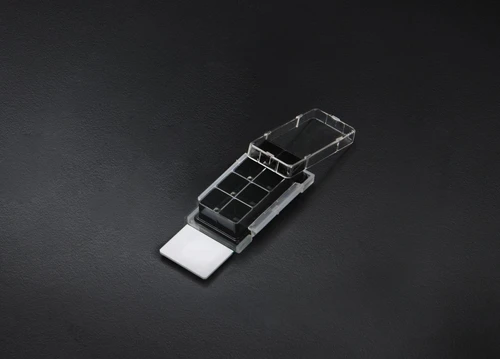 Nest black 8-well cell culture chamber slide with glass base and open clear plastic lid on a dark surface.