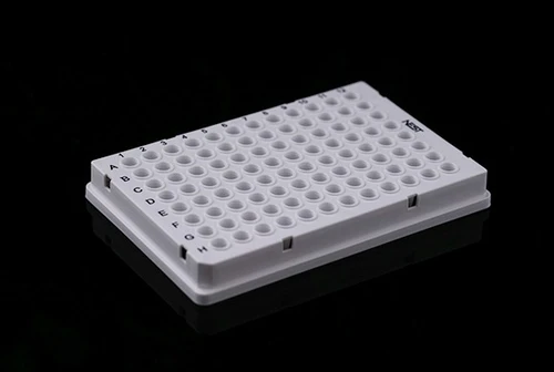Angle view of a white NEST 96-well PCR plate with full skirt on a black surface.