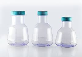 Three clear plastic Erlenmeyer culture flasks with teal screw caps standing in a row on a white surface.