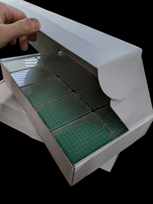 A hand opening a white cardboard case containing multiple racks of green filtered pipette tips.