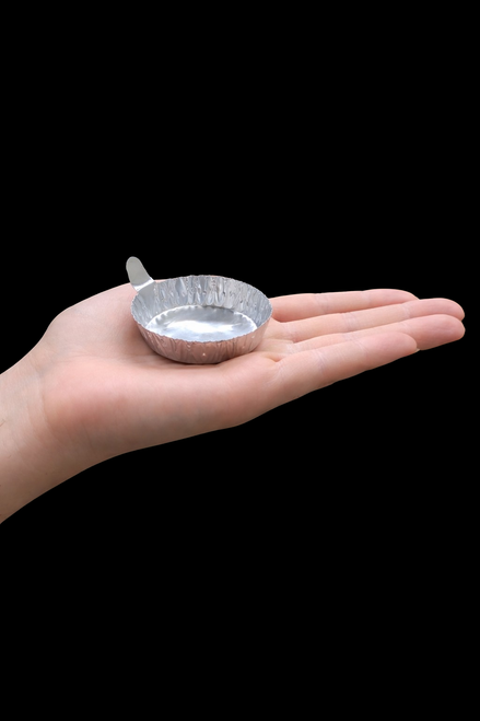 A single, round aluminum weighing pan with a small handle tab resting on an open palm.