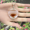 Large round agate jewelry "Dunes of Mars" shown in a model's hand with a garden background.