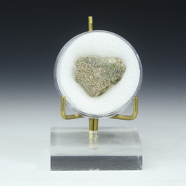 Trinitite atomic glass number 53217, shown front in a disk on a plexiglass riser with gold prongs.