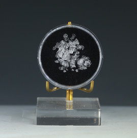 Sassolite mineral in a round black disc from Sasso Pisano hot boric acid springs, Italy, on a display stand.