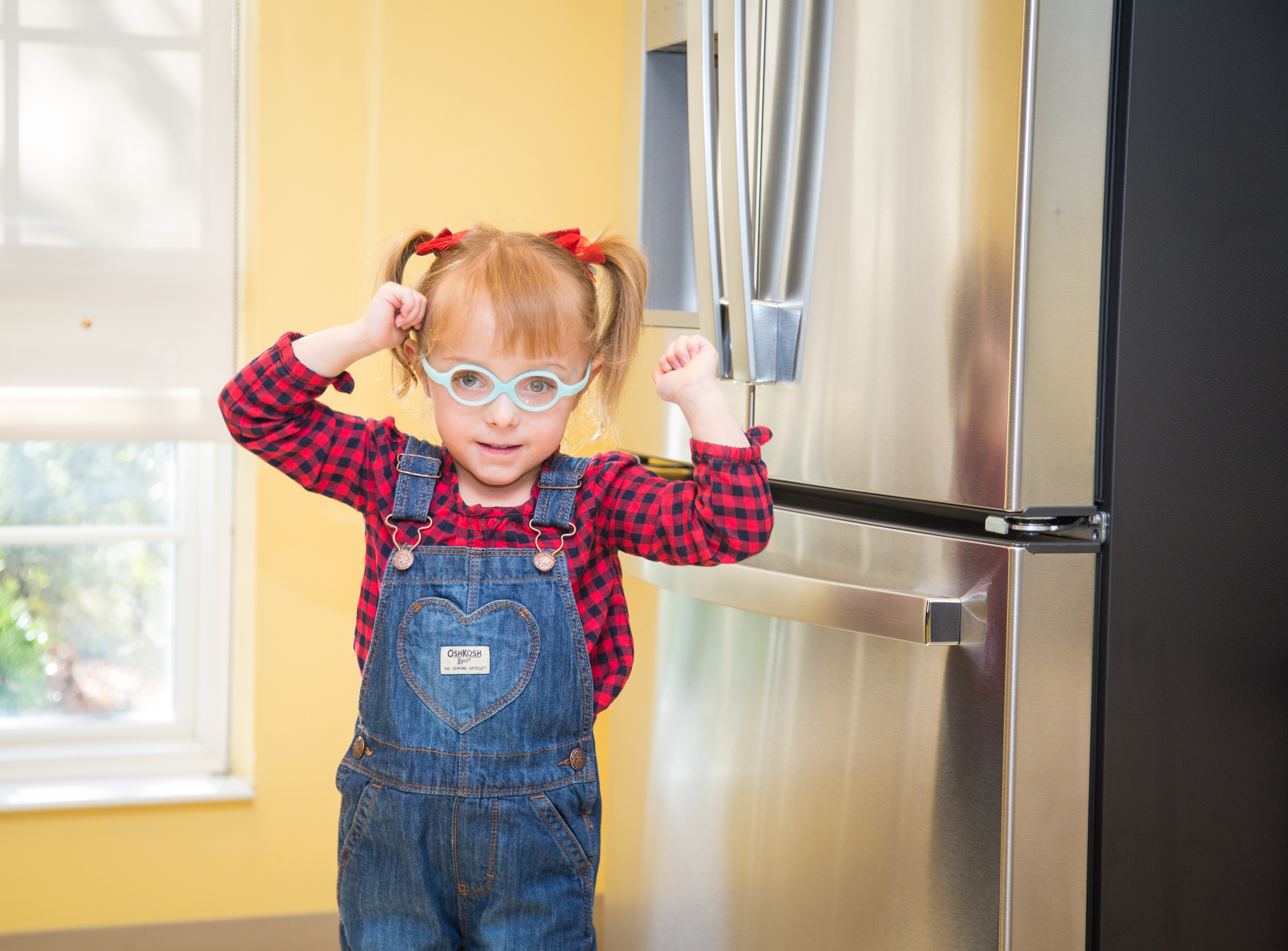 Young girl with glasses flexes her muscles in front of a GE refrigerator