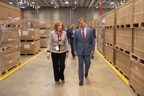 A man and woman walk down an aisle of boxes in a GE warehouse.