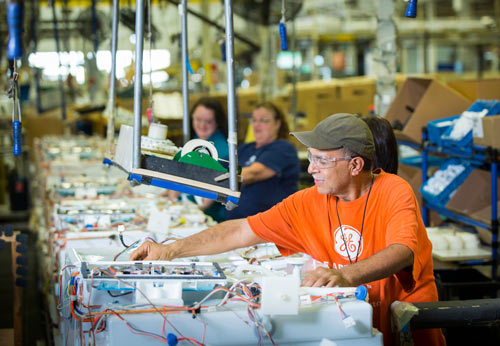 A man in an orange shirt inspects electrical components.