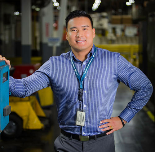 A middle aged Asian man wearing a button down shirt smiles.