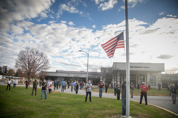 A group of veterans gather socially distanced and wearing face masks to pledge allegiance to the American flag midway on a flag pole.