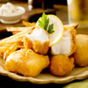 A pile of battered Alaska halibut chunks with fries and lemon slice.