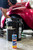 A person in a baseball hat with a beard uses a black bucket that says Flitz to wash a classic red car. A bottle of Flitz Car Wash Soap is in the foreground.