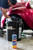 A person in a baseball hat with a beard uses a black bucket that says Flitz to wash a classic red car. A bottle of Flitz Car Wash Soap is in the foreground.