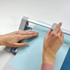 Dahle 507 A4 Self-Sharpening Paper Trimmer Guillotine with Safety Cutting Protection, Blue, in use trimming blue paper with safety features visible.