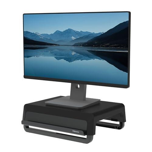 Fellowes Monitor Stand for Desk, a black, ergonomic portable monitor stand with three height settings placed on a black adjustable base, supporting a large flat-screen monitor displaying a scenic mountain landscape and lake.