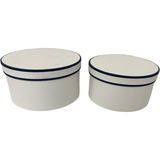 A set of 2 round white hat boxes with navy blue piping.