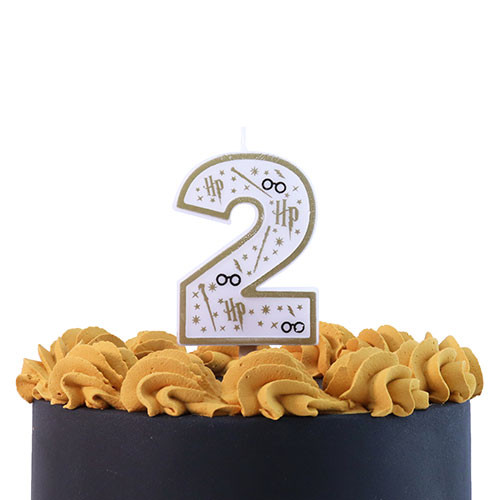 A number two candle with Harry Potter themed design in white, black, and gold, with lightning bolts, wands, stars, and glasses, shown on the top of an iced cake.