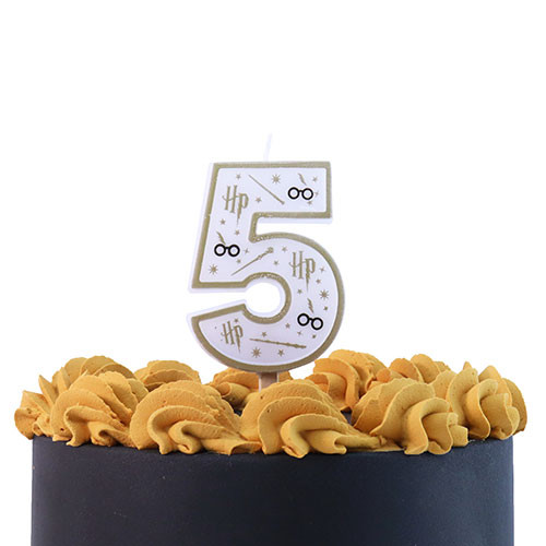 A number five candle with Harry Potter themed design in white, black, and gold, with lightning bolts, wands, stars, and glasses, shown on the top of an iced cake.