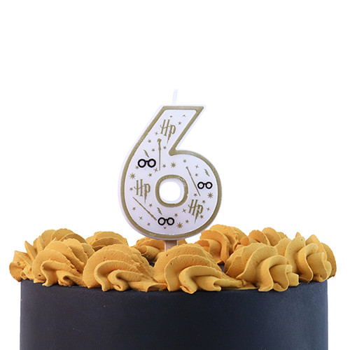 A number six candle with Harry Potter themed design in white, black, and gold, with lightning bolts, wands, stars, and glasses, shown on the top of an iced cake.