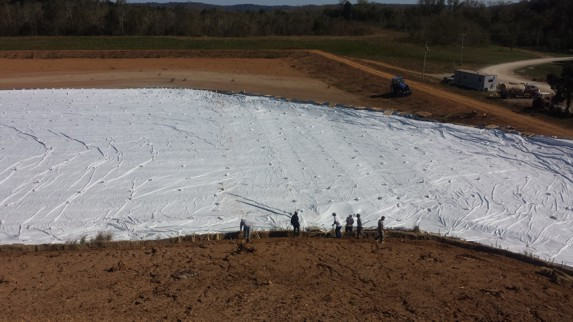 Construction workers install large industrial tarp on landfill in Louisville, showcasing durable industrial fabrics and textiles.