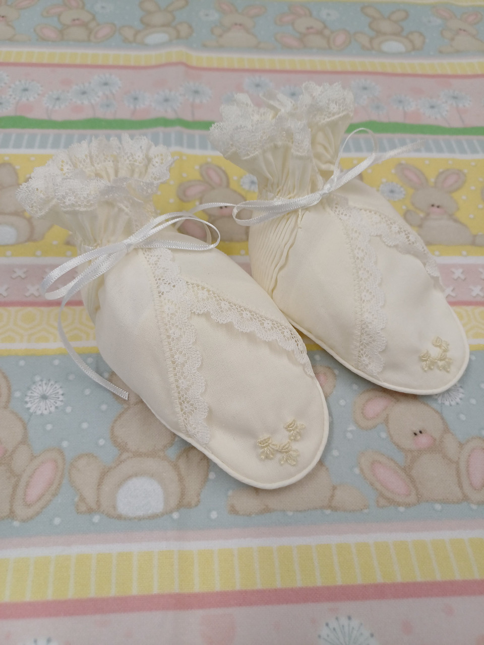 A pretty pair of bootees, Sized to fit 3-6 months, Made in Rice coloured imperial batiste, Wash at 30 degrees, pleated at the back with smocked ribbon insert, Embroidered roses on the toes