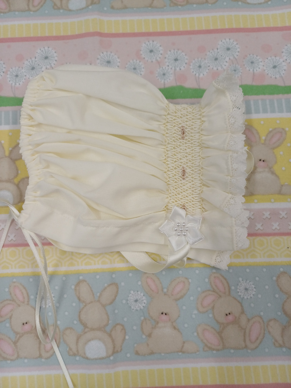 A pretty smocked bonnet, Sized to fit 3-6 months, Made in Rice coloured imperial batiste, Wash at 30 degrees, Draw string at the back for size adjustment,