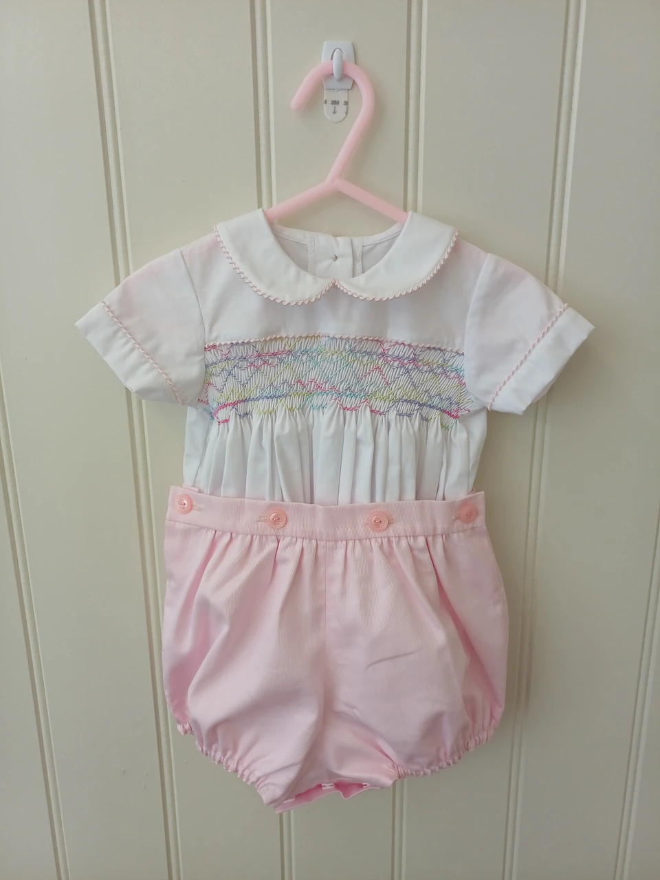 A lovely little button on suit, Size 3-6 month, Multi-coloured hand smocking, Pink whip stitch piping, Pink pique coloured button on pants, Elastic back waistband, Elasticated round the legs, Shirt made from 100% cotton poplin, Pants made from 100% cotton pique, Wash at 30 degrees