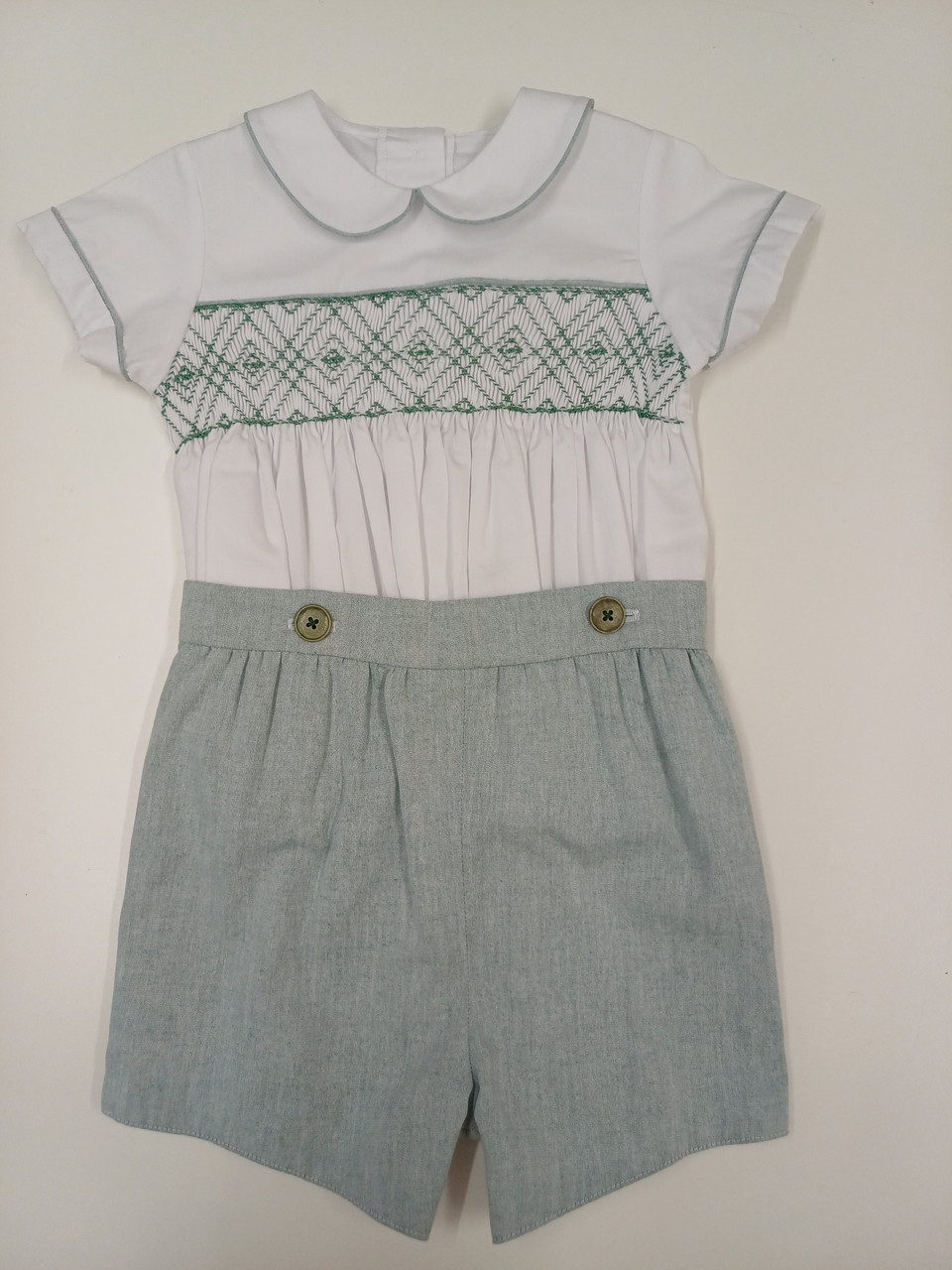 A lovely little button on suit, Size 12-18 month, Green and white coloured hand smocking, Forest Green coloured piping, Forest green coloured button on pants, Elastic back waistband, Elasticated round the back of the legs, Shirt made from 100% cotton poplin, Pants made from 100% sun-washed chambray, Wash at 30 degrees