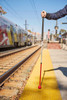 Person holding an All Terrain Cane, strong and lightweight mobility cane for individuals with low vision and blindness standing on a train platform next to train tracks.
