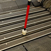 Urban Xplorer mobility cane fully extended with the dome tip cruising across metal and rubber planks in between two rail cars.